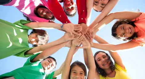 A group of eight children looking down into camera with hands meeting in middle to form a star shape.