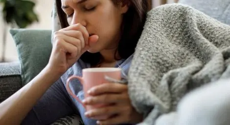 Women holding a warm drink and covering her mouth as she coughs